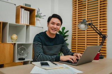 Merkez ofiste dizüstü bilgisayarla çalışan mutlu genç adam.