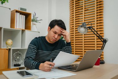 Evrak ve bilgisayarla çalışan stresli genç adam.