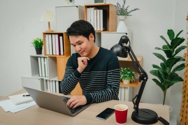 Genç adam evdeki bilgisayarla düşünüyor ve çalışıyor.