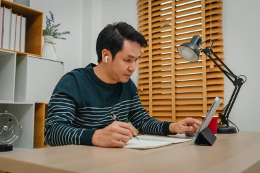 Genç adam internet üzerinden tablet ve kablosuz kulaklıkla ev ofisinde öğreniyor.