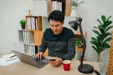 Ofiste akıllı telefon ve dizüstü bilgisayarla çalışan stresli bir adam.