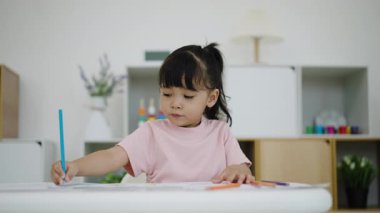 toddler baby girl training to drawing with colored pencil on a desk at home