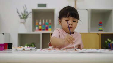 happy toddler girl painting watercolor in paper at home