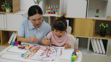 happy mother and toddler girl painting watercolor in a paper at home