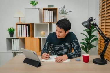 Genç adam internet üzerinden tablet ve kablosuz kulaklıkla ev ofisinde öğreniyor.