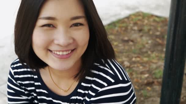 Esen rüzgar seyir siyah saçlı gülümseyen genç Asya kadın portresi kapatın ve arka plan yavaş hareket bulanıklığı — Stok video