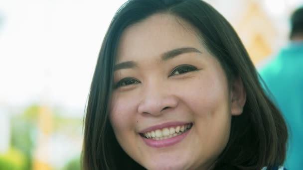 Portrét mladé ženy Asie usmívající se s černými vlasy vlající ve větru při pohledu zblízka a rozostřit pozadí Zpomalený pohyb — Stock video