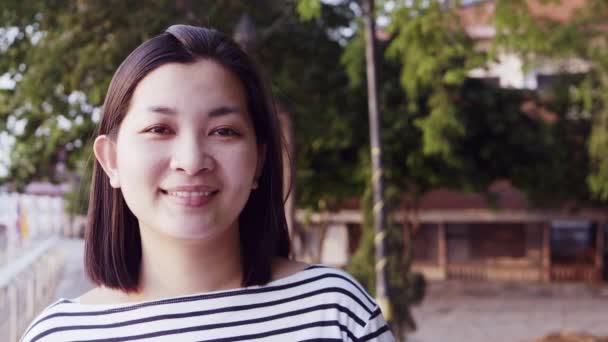 Close up retrato da jovem mulher asiática sorrindo com o cabelo preto soprando no vento olhando para o pôr do sol perto do rio. Mulher vestindo é xadrez camisa preto e branco com cena Slow Motion . — Vídeo de Stock