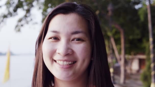 Close up retrato da jovem mulher asiática sorrindo com o cabelo preto soprando no vento olhando para o pôr do sol perto do rio. Mulher vestindo é xadrez camisa preto e branco com cena Slow Motion . — Vídeo de Stock