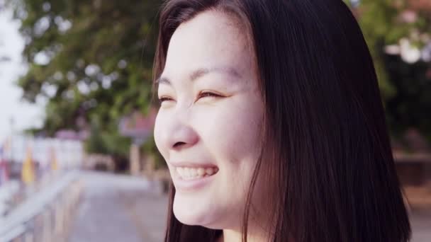 Close up retrato da jovem mulher asiática sorrindo com o cabelo preto soprando no vento olhando para o pôr do sol perto do rio. Mulher vestindo é xadrez camisa preto e branco com cena Slow Motion . — Vídeo de Stock