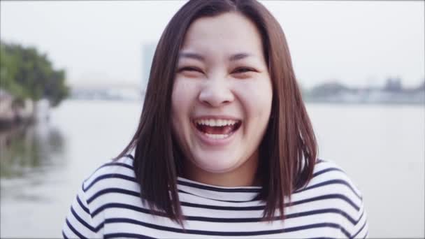 Close up portrait of Young Asian Woman smiling with Black hair blowing in wind looking at the sunset near the river. Woman wearing is plaid shirt black and white with Slow Motion scene. — Stock Video