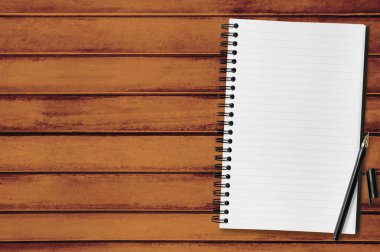 Ahşap ofis masasının üstünde kalem olan boş bir defter sayfası. Üst manzara, düz uzanma.