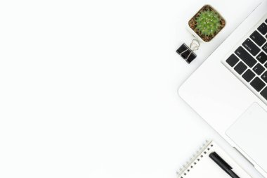 Laptop ve malzemelerle dolu beyaz, minimal ofis masası. Kopyalama alanı olan üst görünüm, düz yatay.