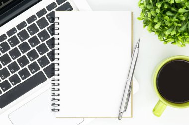 Beyaz ofis masasının ortasında boş bir defter sayfası. Üst manzara, düz uzanma.