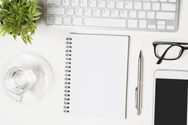 Boş defter sayfası beyaz ofis masasının üstünde. Üst manzara, düz uzanma.