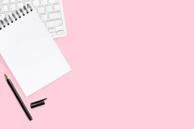 Boş defter, kalem ve bilgisayar klavyeli pembe pastel ofis masası. Kopyalama alanı olan üst görünüm, düz yatay.