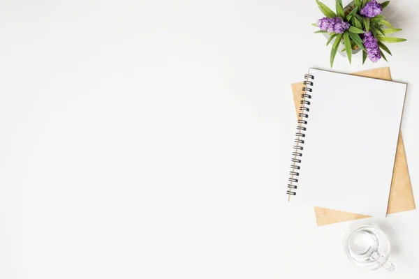 Minimal white office desk table with notebooks, glass of drinking water and flower pot. Top view with copy space, flat lay.