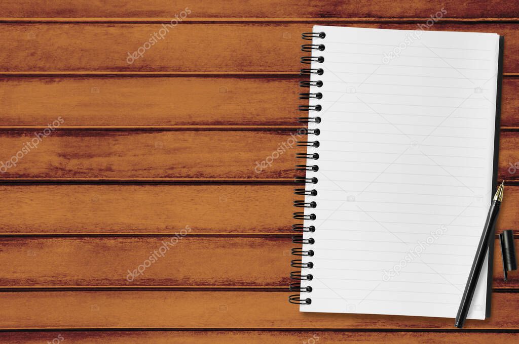 Blank notebook page with pen on top of wood office desk table. Top view, flat lay.