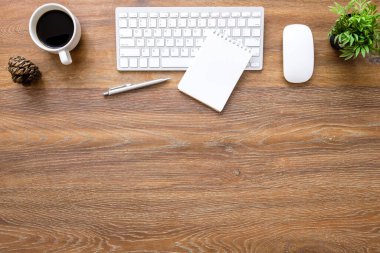 Ahşap ofis masasında fareli bilgisayar klavyesi, boş defter, bir fincan kahve ve malzeme. Kopyalama alanı olan üst görünüm, düz yatay.