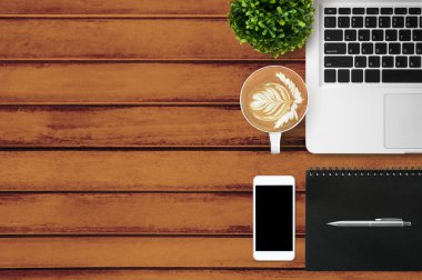 Diz üstü bilgisayarı, akıllı telefonu ve malzemeleri olan ahşap ofis masası. Üst manzara, düz uzanma.