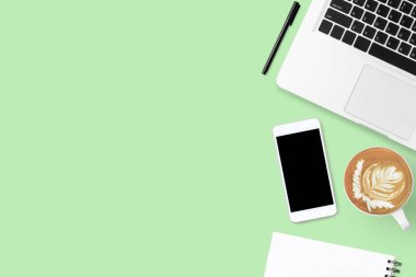 Laptop bilgisayarı, akıllı telefon, kahve ve malzemelerle dolu yeşil pastel ofis masası. Kopyalama alanı olan üst görünüm, düz yatay.