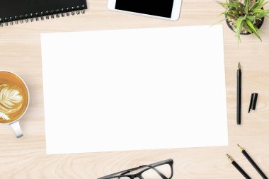 Boş bir a4 kâğıdı ahşap ofis masasının üstünde malzemelerle birlikte. Üst manzara, düz uzanma.