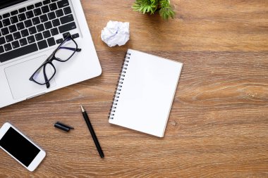 Boş defter, bilgisayar gereçleri ve malzemeleri olan ahşap ofis masası. Kopyalama alanı olan üst görünüm, düz yatay.