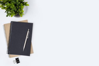 Not defterleri, kalem ve bitkilerle dolu beyaz ofis masası. Kopyalama alanı olan üst görünüm, düz yatay.