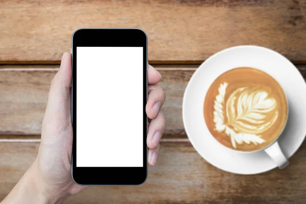 Hand is holding smartphone with blank screen over the table of coffee cafe.