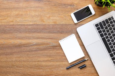 Defter, akıllı telefon, laptop ve sup içeren ahşap ofis masası.