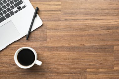 Laptop, kalem ve kahve dolu ahşap ofis masası. Kopyalama alanı olan üst görünüm, düz yatay.