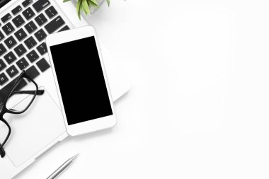 Boş ekranlı beyaz akıllı telefon ofisteki dizüstü bilgisayarın üstünde.