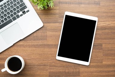 Boş ekran tabletli ahşap masa, dizüstü bilgisayar ve bir fincan kahve. Üst manzara, düz uzanma.