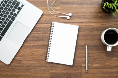 Boş defter ahşap ofis masasının üstünde malzemelerle birlikte. Kopyalama alanı olan üst görünüm, düz yatay.