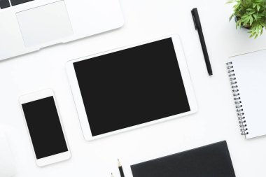 Beyaz tablet ve boş ekranlı akıllı telefon beyaz ofis masasının üstünde. Üst manzara, düz uzanma.