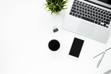 Akıllı telefon, dizüstü bilgisayar ve malzemelerle dolu beyaz ofis masası. Kopyalama alanı olan üst görünüm, düz yatay.