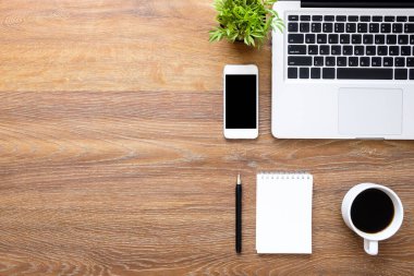 Defter, akıllı telefon, laptop ve sup içeren ahşap ofis masası.