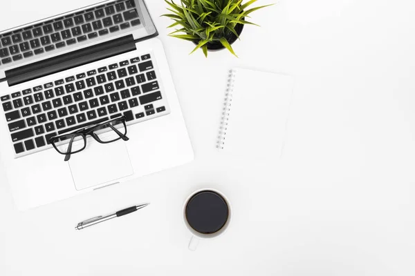 Blank notebook is on top of white office desk table with laptop, coffee cup and office supplies. Top view with copy space, flat lay.