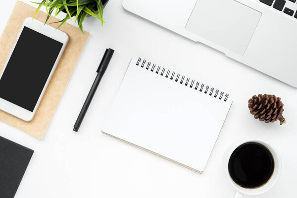 Чистый блокнот находится в середине белого стола офиса стол с принадлежностями. Вид сверху, плоский.