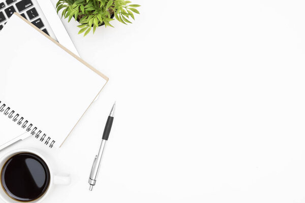 Белый стол с чистым блокнотом, ноутбуком, чашкой кофе и принадлежностями. Вид сверху, плоский.