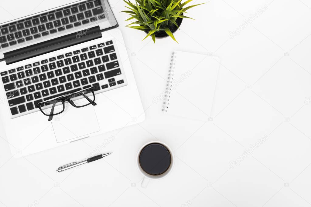 Blank notebook is on top of white office desk table with laptop, coffee cup and office supplies. Top view with copy space, flat lay.