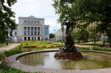Riga, Letonya - 27 Temmuz 2013: Latvian National Opera Binası ve çeşme ile ön planda bir bronz heykel