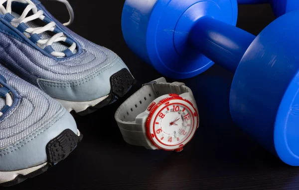 Baskets, haltères et une montre sur un fond sombre — Photo