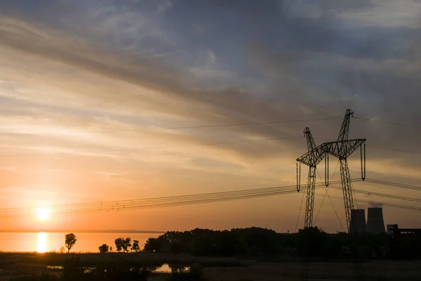 power line support against the background of a red sunset on the water