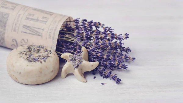 天然の手作り石鹸のピースをスクラブします Coldprocess ラベンダーの香りのエッセンシャル オイル ビンテージ新聞で光の木製の表面の乾燥ラベンダーの花束 紫の調子を整えます 小石と星型 — ストック写真