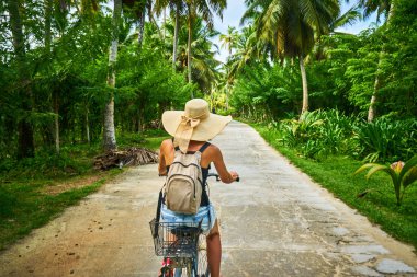 Bisikletli bir kadın vanilya tarlalarını, dique adasını geçiyor.