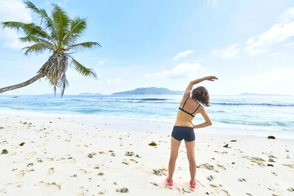 Mujer joven estirándose antes del entrenamiento en la playa tropical, sey Imágenes De Stock Sin Royalties Gratis