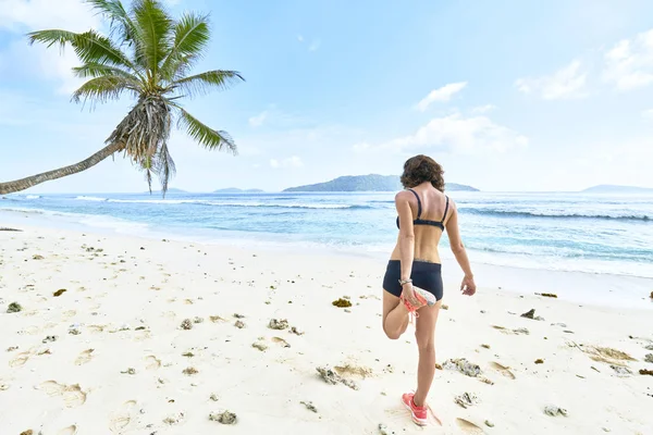 Genç bir kadın tropikal plajda egzersiz yapmadan önce geriniyor.
