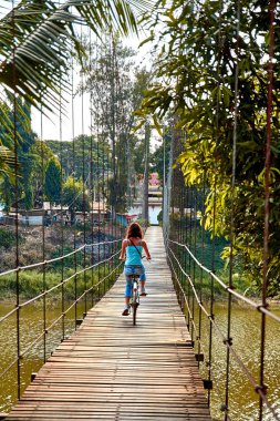 Si Satchanalai, Sukhothai Tayland 'da asma köprüden bisikletle geçen bir kadın.