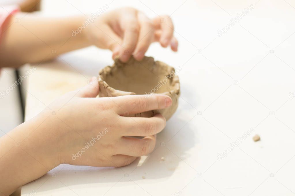 Children make clay. The hands of the child hold the clay. Light room. Clay dishes